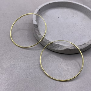 Könnte beinhalten: Ein Paar goldene Creolen. Die Ohrringe sind schlicht und elegant und würden eine großartige Ergänzung für jede Schmucksammlung sein.
