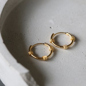May include: A pair of gold hoop earrings with a textured knotted design. The earrings are small and delicate.
