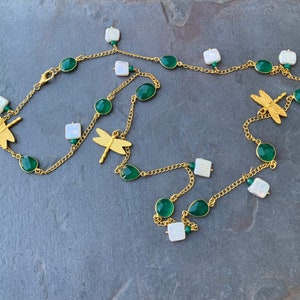 May include: A gold chain necklace with green and white gemstone beads and dragonfly charms.