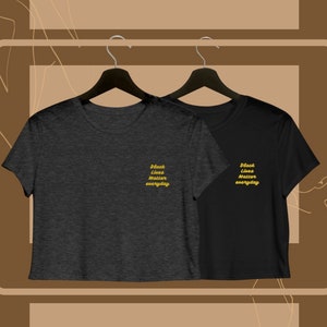 Può includere: Due t-shirt a maniche corte crop. Le magliette sono nere e grigio scuro. Il testo "Black Lives Matter everyday" è stampato in oro su entrambe le magliette.