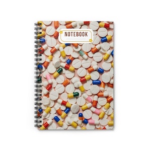 May include: Spiral-bound notebook with a cover featuring a pattern of white pills and colorful capsules on a pink background. The word "NOTEBOOK" is displayed in a rectangular box with floral accents.