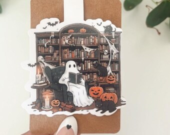 May include: A sticker featuring a ghost reading a book in a library with a fireplace, candles, and pumpkins. There are also black cats and bats in the illustration.