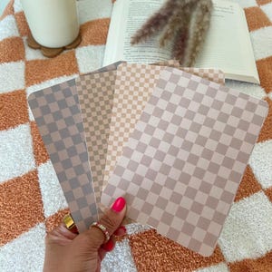 Può includere: Quattro carte con motivo a scacchi in tonalità di marrone e beige. Le carte sono disposte a ventaglio e sono tenute in una mano.