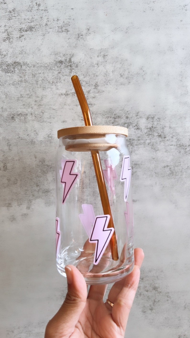May include: A clear glass bottle with a wooden lid and a pink lightning bolt design. The bottle has a brown straw sticking out of the top.