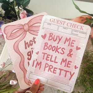 May include: Two pink paper items with text. One has a bow graphic and the words "hot girl". The other says "Buy me books & tell me I'm pretty" in pink text. The items are designed to look like a guest check.