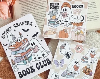 Op de afbeelding: Drie decoratieve stickers met boeken als thema met spookachtige personages die boeken lezen. Eén sticker leest "Spooky Readers Book Club" met vleermuizen en kaarsen. Een andere zegt "Read More Books" met een pompoen en een croissant. De derde sticker heeft een bloem en een zwarte kat.