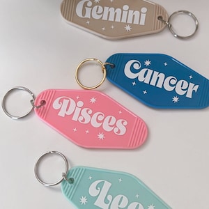 May include: Four colorful keychains shaped like motel room keys with the zodiac signs Gemini, Cancer, Pisces, and Leo printed on them in white.