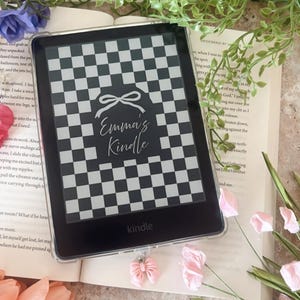 May include: A Kindle e-reader with a black and white checkered design cover, featuring the text "Emma's Kindle" in a script font. The e-reader is surrounded by a book, flowers, and decorative elements.