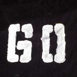 May include: White stencil letters "GO" on a black background.