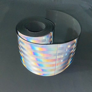 Puede incluir: Un rollo de cinta reflectante holográfica iridiscente con rayas plateadas y arcoíris.