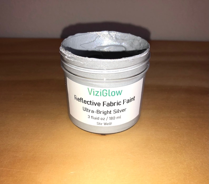 May include: A small jar of silver reflective fabric paint labeled "ViziGlow Reflective Fabric Paint Ultra-Bright Silver 3 fluid oz / 180 ml Stir Well!"