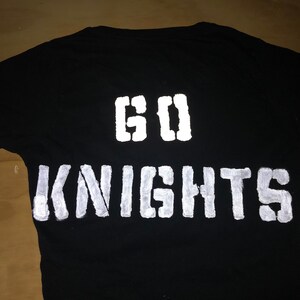 May include: Black t-shirt with white reflective paint, featuring the words "GO KNIGHTS" on the back.