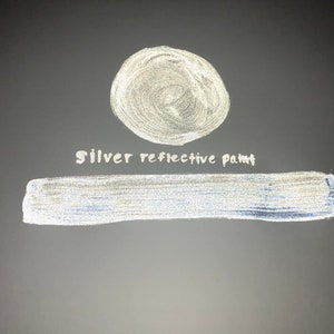 May include: A silver reflective paint sample. The paint is shown in a circle and a long rectangle. The text "Silver reflective paint" is written in white below the circle.
