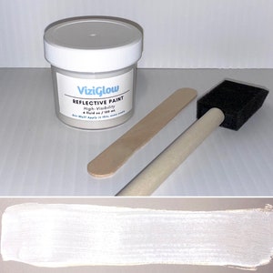 May include: A small white jar of reflective paint with a white lid and a black and white label that reads "ViziGlow Reflective Paint High-Visibility 4 fluid oz / 120 ml Stir Well! Apply in thin, even coats". The jar is accompanied by a wooden paint stirrer and a foam paint brush.