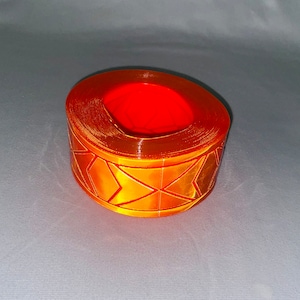 Puede incluir: Cinta reflectante naranja con un patrón de diamante. La cinta está enrollada en un círculo y tiene un diámetro de aproximadamente 5 cm.
