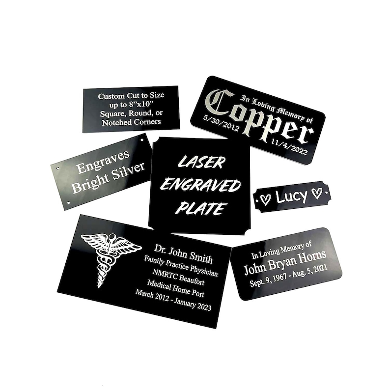 K&ouml;nnte beinhalten: Eine Sammlung von schwarz lasergravierten Platten mit wei&szlig;em Text. Einige Platten enthalten Texte wie "Custom Cut to Size", "Engraves Bright Silver" und "Laser Engraved Plate". Andere Platten enthalten Namen und Daten.