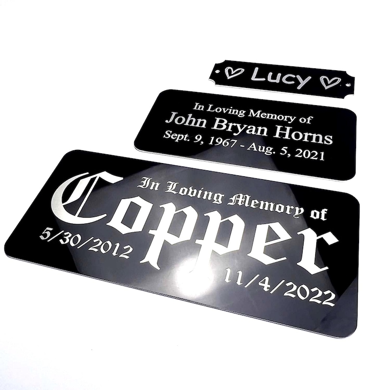 K&ouml;nnte beinhalten: Schwarze Gedenktafeln mit wei&szlig;em Text. Eine Tafel tr&auml;gt die Aufschrift "Lucy" mit Herzen. Eine andere lautet "In Loving Memory of John Bryan Horns" mit Daten. Die gr&ouml;&szlig;te Tafel tr&auml;gt die Aufschrift "In Loving Memory of Copper" mit Daten.