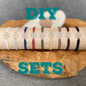 Puede incluir: Sets de pulseras DIY con dijes plateados en varios colores, incluyendo blanco, azul marino, rojo, verde, beige, marrón y negro. Las pulseras se muestran sobre una superficie de madera.