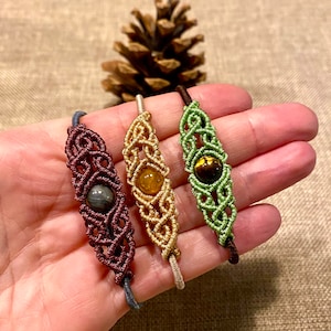 Peut inclure: Trois bracelets en macramé faits à la main avec des cordons de différentes couleurs et des perles de pierres précieuses. Les bracelets sont marron, or et vert.