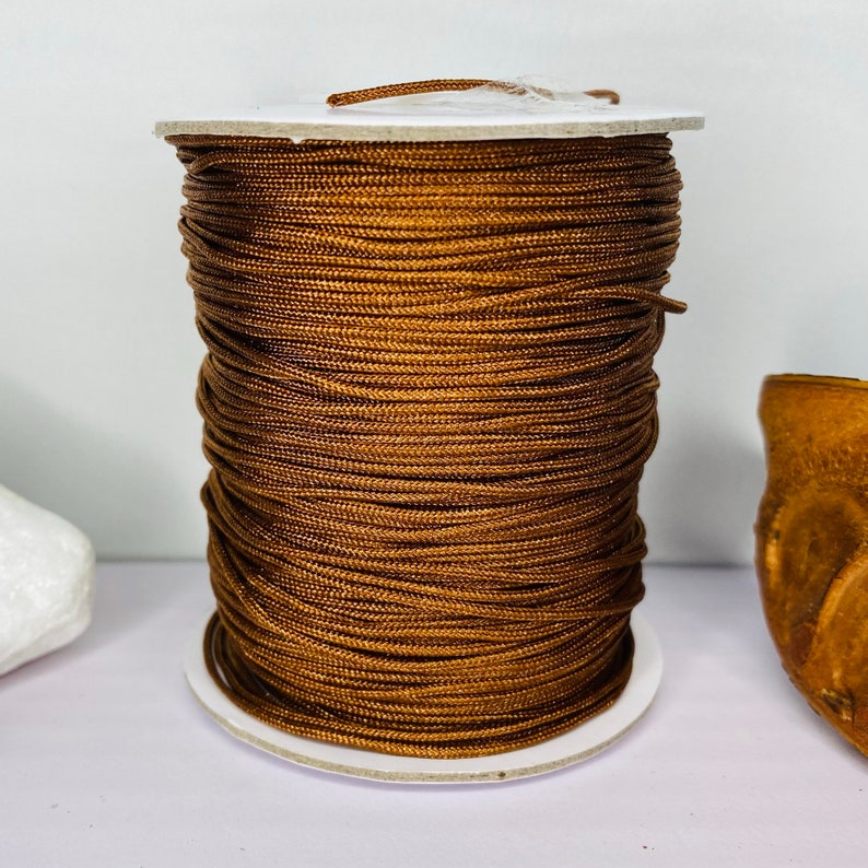 May include: A spool of brown cord wound around a white cardboard tube. The cord is tightly wound and appears to be made of a smooth, synthetic material.
