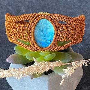 Könnte beinhalten: Ein braunes Makramee-Armband mit einem blauen Labradorit-Edelstein. Das Armband ist mit goldenen Perlen verziert.