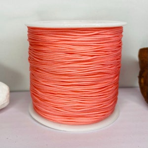 May include: A spool of peach-colored cord wound around a white plastic bobbin.