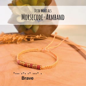 Op de afbeelding: Een gevlochten armband met kleine cilindrische kralen in goud en roze. De armband is vastgebonden met een lichtgeel koord. Het woord "Brave" staat eronder. De tekst "DEIN WORT ALS MORSECODE-ARMBAND" staat erboven.