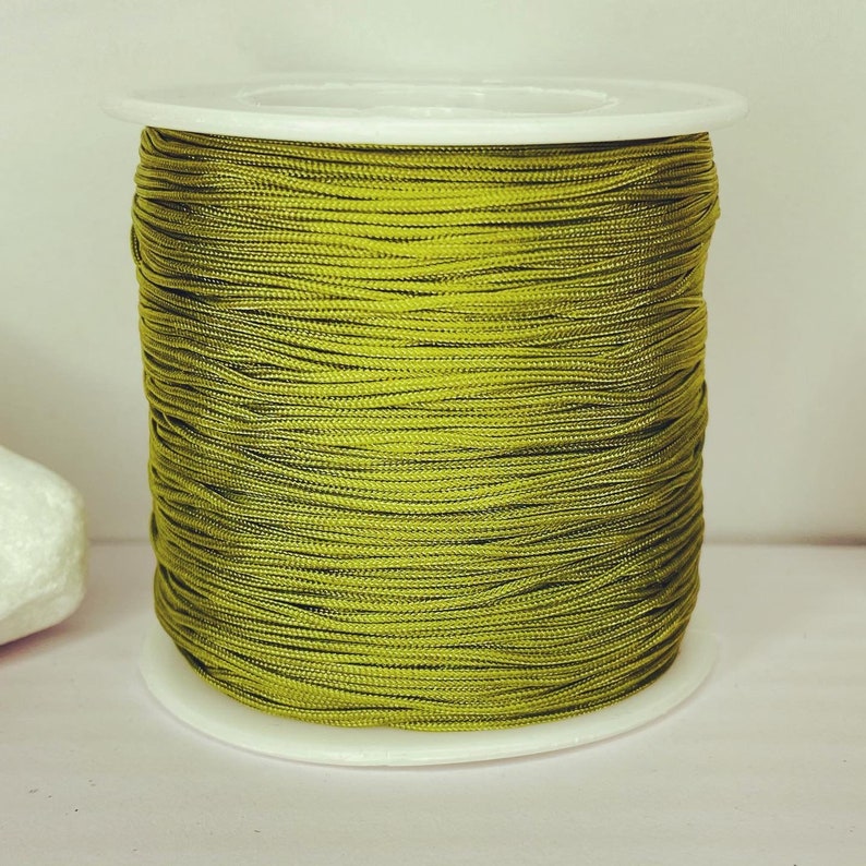 May include: A spool of olive green waxed cord, wound tightly on a white plastic bobbin.