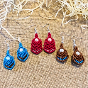 Può includere: Tre paia di orecchini in macramè fatti a mano con accenti di perle. Gli orecchini sono in tonalità di blu, marrone e rosso.