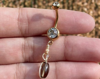 May include: Gold belly button ring with a clear crystal and a dangling brown stone charm.