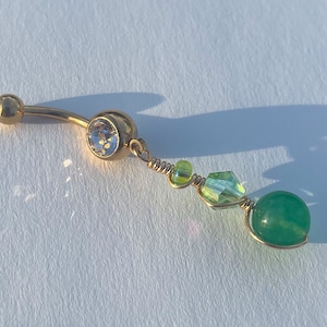 May include: Gold belly button ring with a clear crystal and a dangling green stone.
