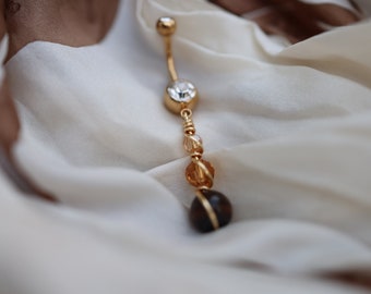 May include: Gold body jewelry with a clear crystal and brown beads.