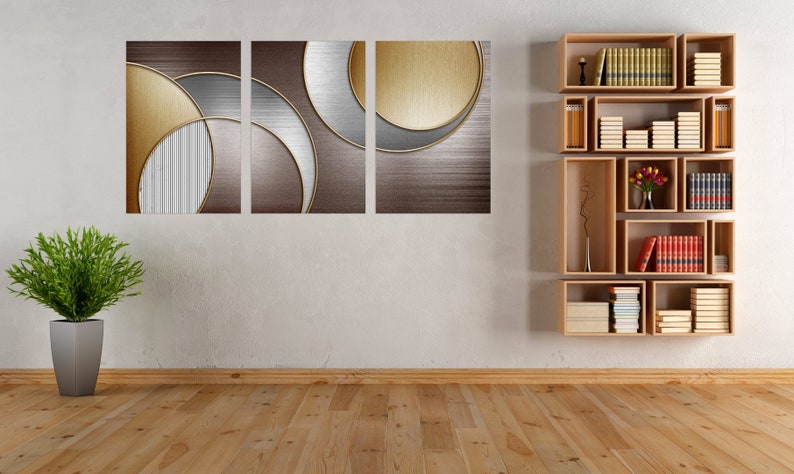May include: A modern abstract art print with geometric shapes in gold, silver, and brown tones. The print is displayed on a white wall above a wooden bookshelf with books and decorative items.