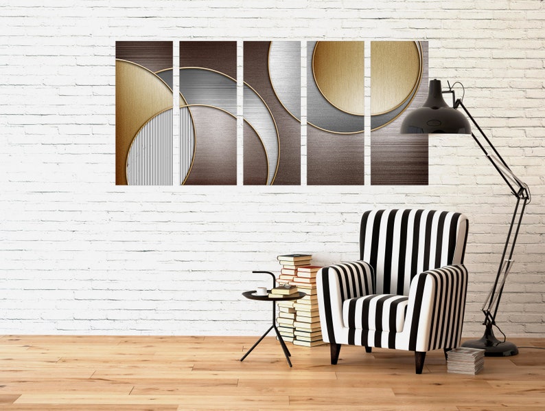 May include: A set of five abstract art prints with geometric shapes in shades of gold, brown, and gray. The prints are arranged in a row on a white brick wall above a black and white striped armchair.