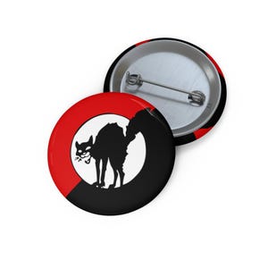 May include: Two round buttons with a black cat silhouette inside a red circle on a black background. One button is face up, the other is face down, showing the pin back.