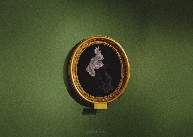 May include: An oval-shaped gold-toned frame containing a black background with a white illustration of a fish swimming downward. The frame features intricate decorative carvings along its edge and a small rectangular gold-toned plaque at the bottom.