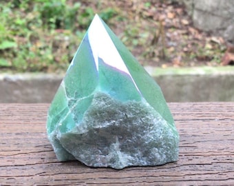 May include: A green crystal point with a polished, smooth top section and a rough, textured base. The stone displays varying shades of translucent and opaque green with white inclusions. The text LIBRA CRYSTALS is visible.