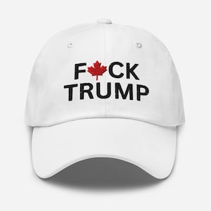 May include: White baseball cap with black embroidered text that reads "F*CK TRUMP" with a red maple leaf in the middle of the word "F*CK".