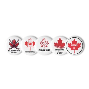 May include: Five white circular badges with red maple leaf designs. The badges feature text including "Elbows Up", "Not for Sale", and "Strong and Free". One badge has a maple leaf with crossed hockey sticks.