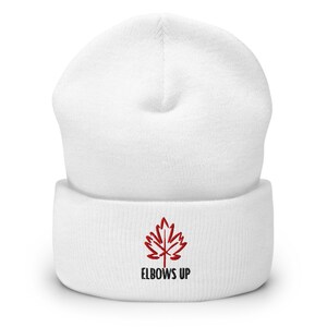 May include: White knitted beanie with a red maple leaf and the text "ELBOWS UP" embroidered on the front.