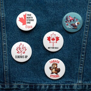 Peut inclure: Cinq épingles rondes blanches avec différents motifs sur le thème canadien. Les épingles présentent une feuille d'érable rouge, un castor, un pygargue à tête blanche et le texte "True North Strong and Free" et "Elbows Up".