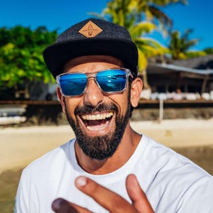 Nahaufnahme eines lachenden Mannes mit Sonnenbrille, der die Snapback Cap trägt. Die Freude und der Lifestyle-Charakter der Cap stehen im Fokus.