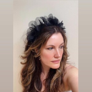 May include: A black headband with large, layered fabric flowers. The headband is worn by a person with long, brown hair.