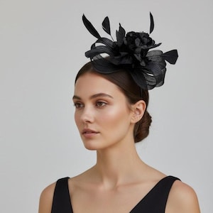 Puede incluir: Tocado negro con diseño floral y plumas. El tocado se lleva en la cabeza y está hecho de un material oscuro. La mujer de la imagen lleva un vestido negro.