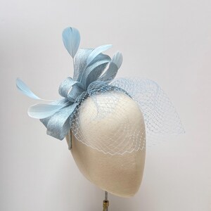 May include: A light blue headband with a bow and feathers. The headband is decorated with a light blue veil.
