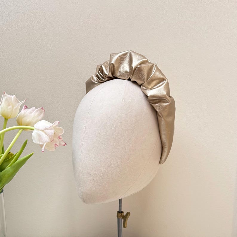 May include: A gold-colored headband made of faux leather with a gathered, ruffled design.