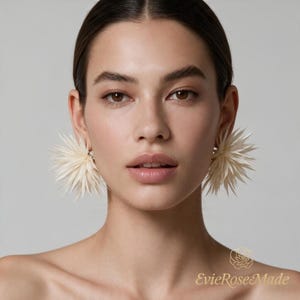 May include: A pair of off-white, spiky, starburst-shaped earrings with a textured, layered petal design. The earrings feature a radial arrangement of pointed elements extending outward from a central point. The text EvieRoseMade is visible.