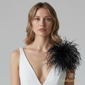 May include: A white sleeveless top featuring a deep V-neckline and a large, voluminous black feather accent attached to the left shoulder. The garment is plain white with a clean, structured design and a prominent dark plume detail.