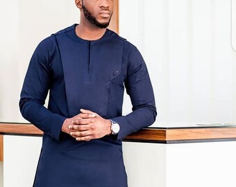 May include: A navy blue tunic-style shirt with long sleeves and a unique asymmetrical design. The shirt features a small pocket and a mandarin collar. The sleeves have buttoned cuffs. A wristwatch with a silver band is visible.