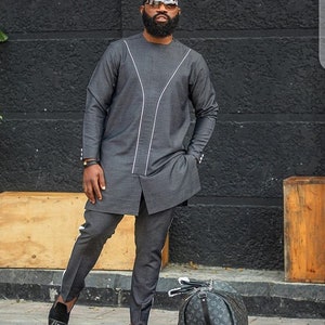 May include: A dark grey two-piece suit with white accent lines. The long-sleeved top has a split hem and the trousers have a white stripe down the side. The outfit is paired with black shoes and a patterned holdall.
